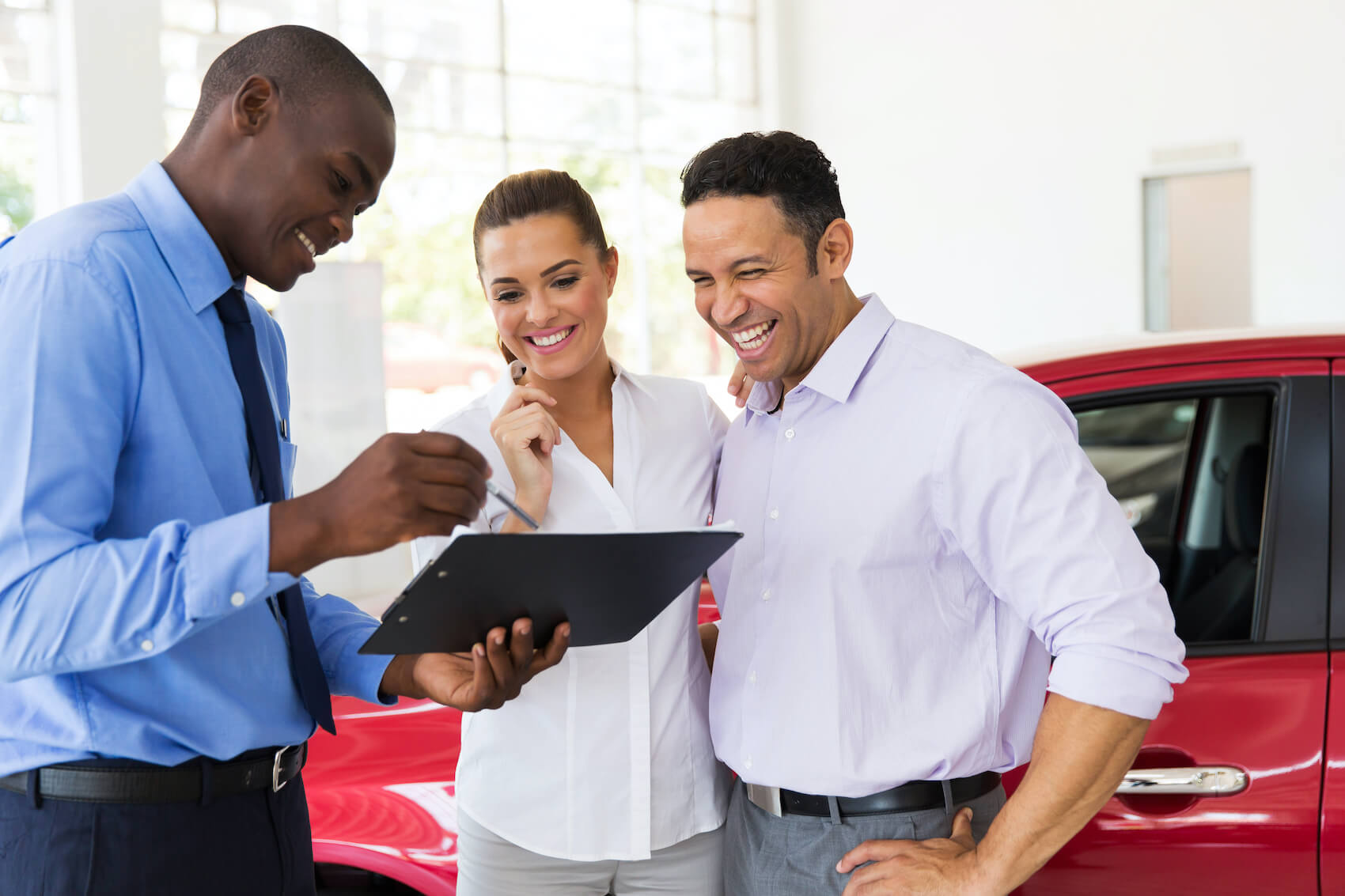 Sales person with couple going over financing paperwork in front of red car