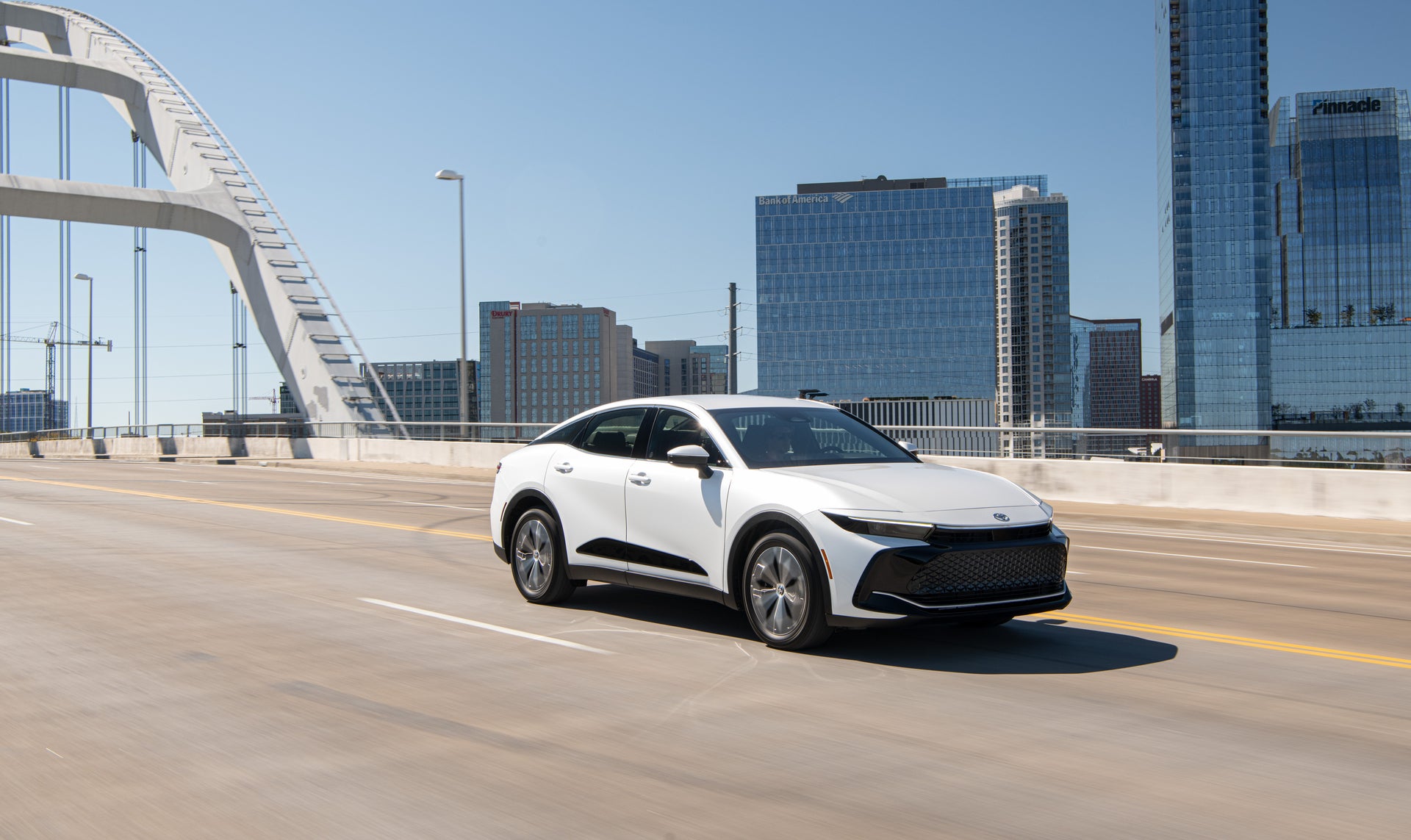 a new white 2026 toyota crown driving with the city in the back ground
