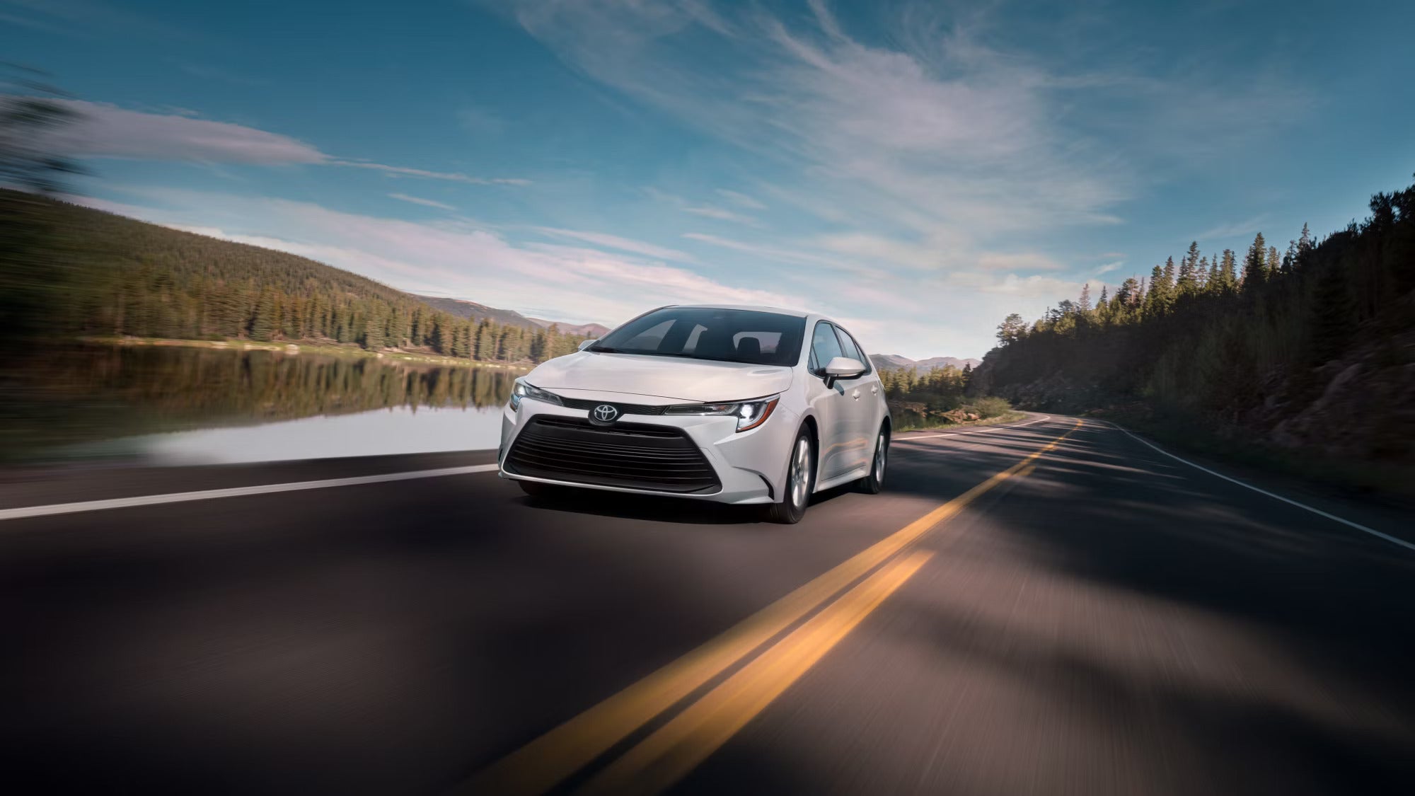 a white toyota corolla driving on a paved road next to a lake