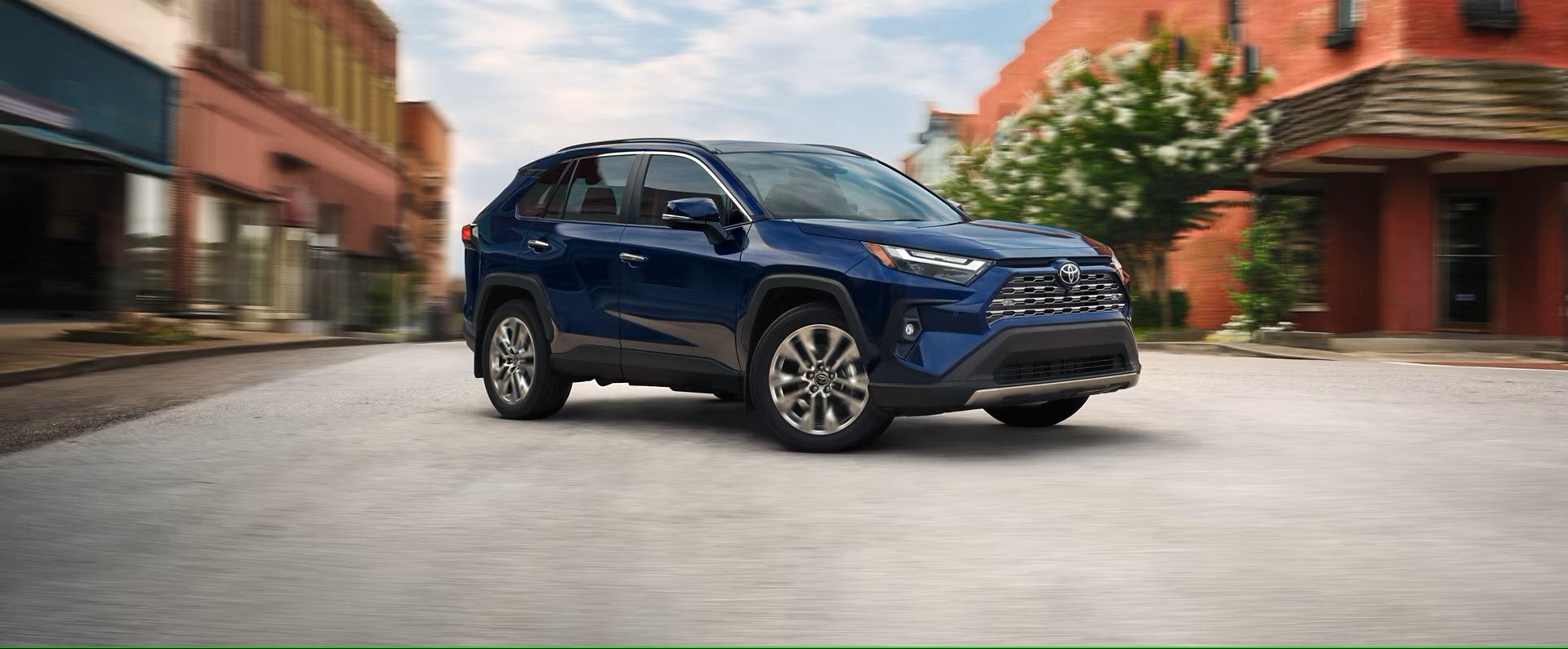 a blue 2025 toyota rav4 suv driving on a paved road in front of old city buildings