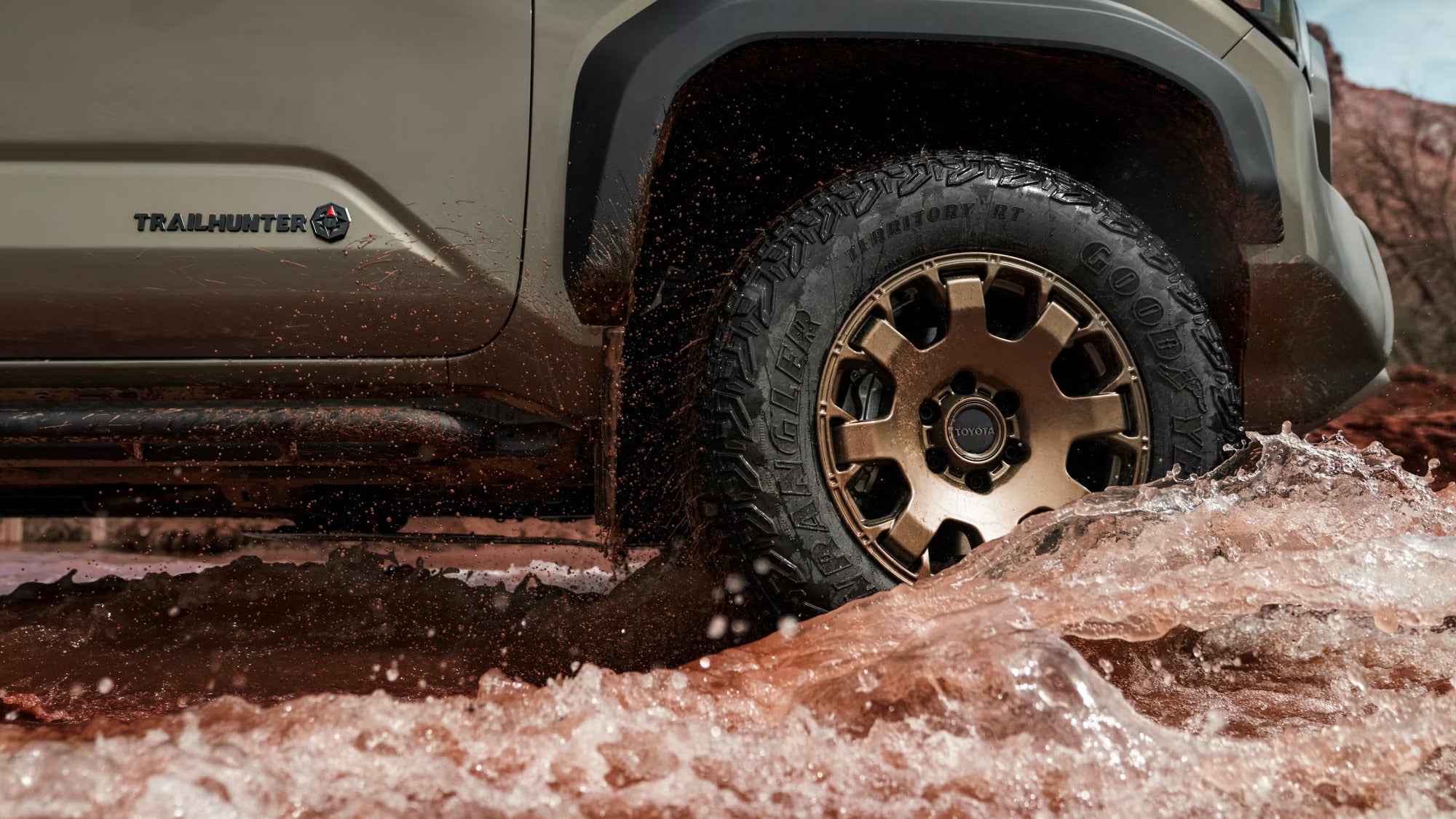 Close-up of a Toyota truck's tire splashing through water on a rough off-road trail.
