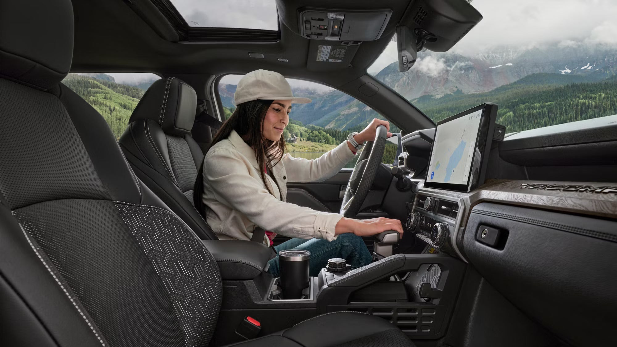 Driver enjoying the 2025 Toyota Tacoma interior with advanced tech, scenic mountain backdrop visible through panoramic windows.
