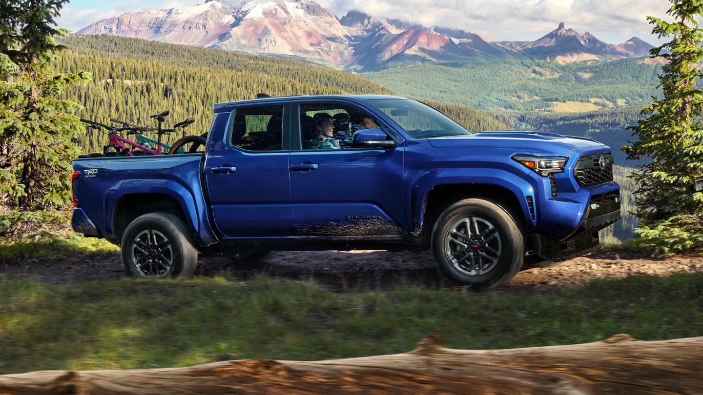 Two Toyota pickup trucks parked on rugged terrain with a scenic canyon backdrop under a partly cloudy sky.