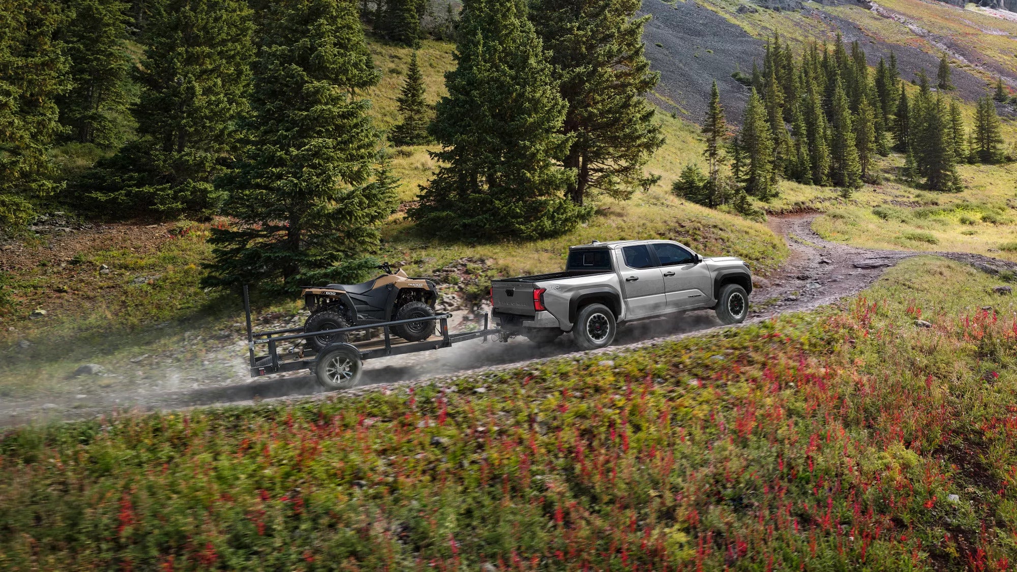 A gray truck pulling a trailer on a dirt road.