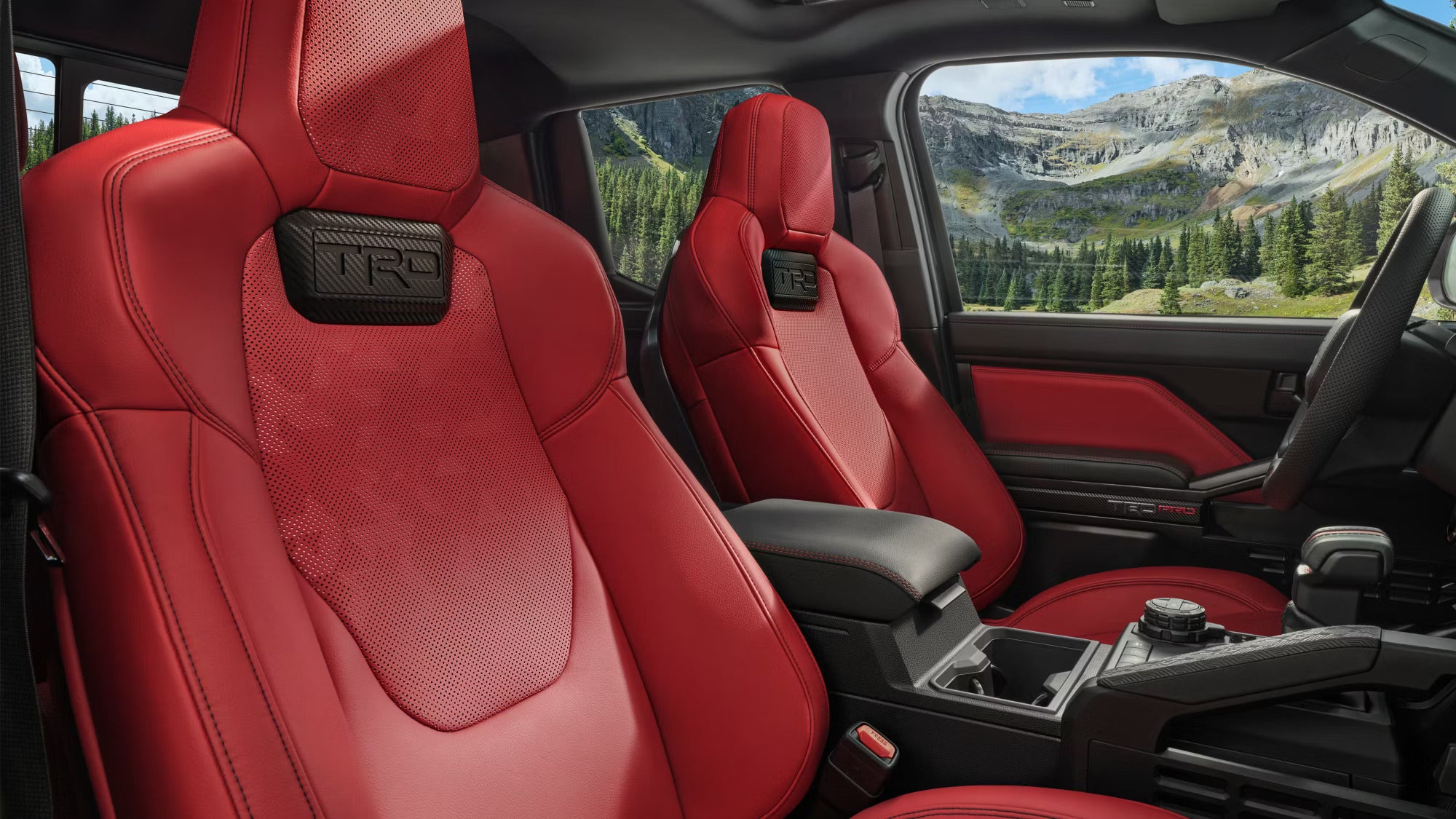 Interior view of a Toyota truck with red TRD leather seats against a scenic mountain background.