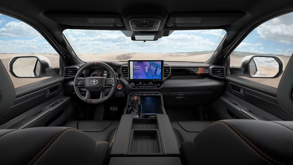 Front interior view of the 2025 Toyota Tundra with a large infotainment screen and panoramic desert landscape